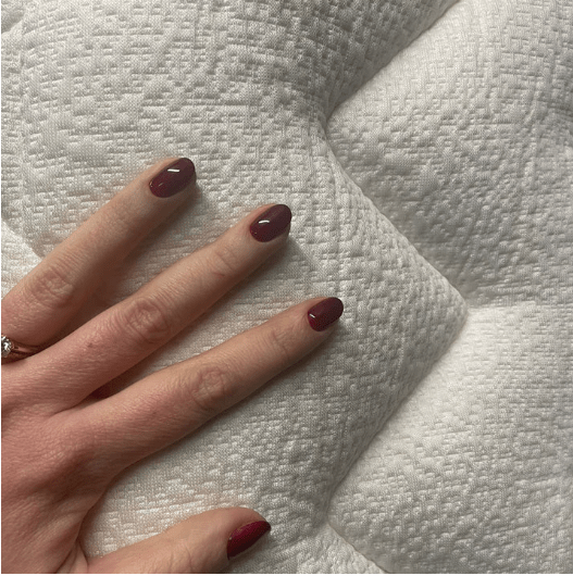 A hand with dark brown nails rests on a white quilted mattress.