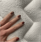 A hand with dark brown nails rests on a white quilted mattress.