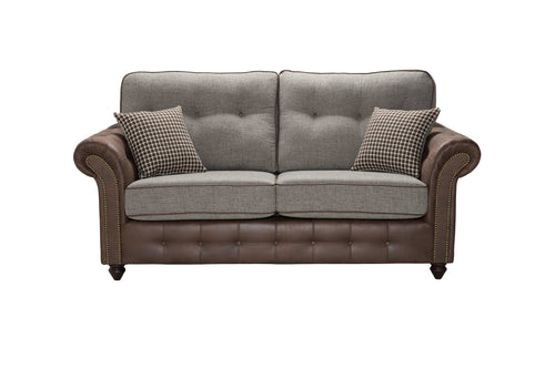 A two-tone sofa with brown leather and grey fabric, featuring decorative studs and two patterned throw pillows.