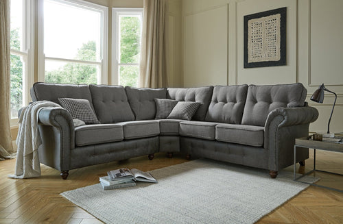 A grey tufted sectional sofa with decorative studs and throw blanket.