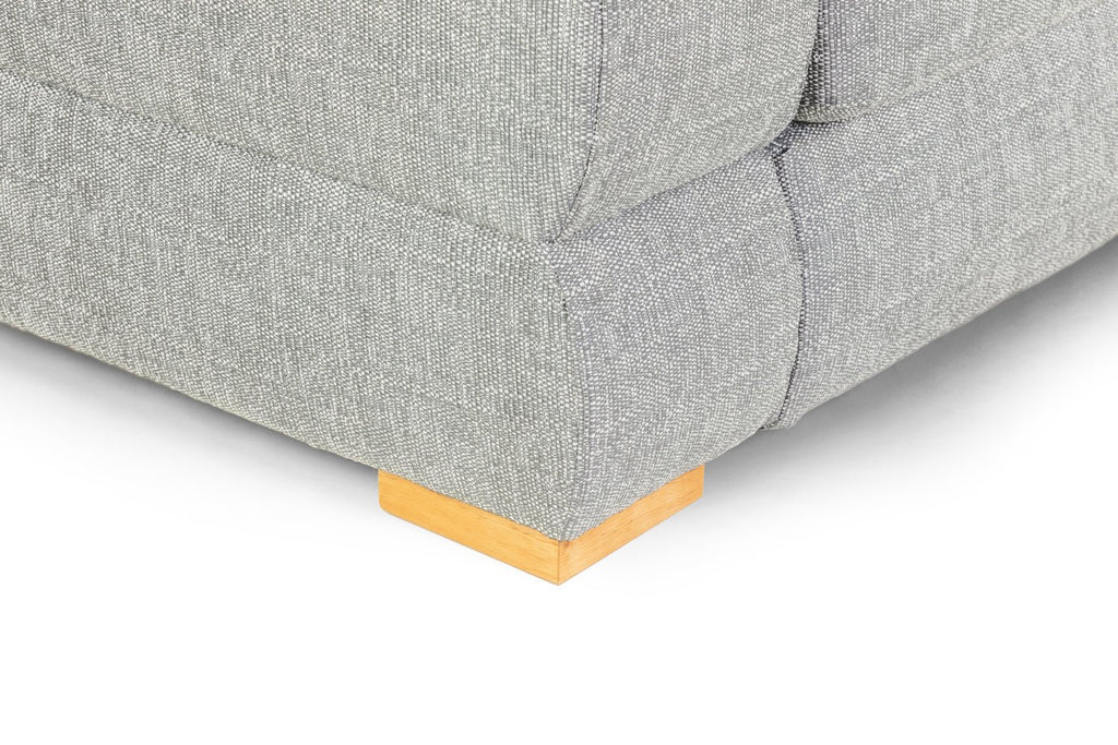 Close-up of a grey fabric sofa corner with a wooden block foot.