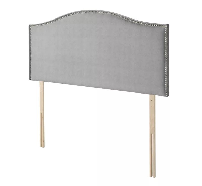 A grey fabric headboard with nailhead trim and wooden legs.