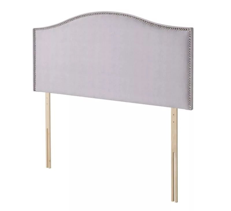 A light gray upholstered headboard with silver nailhead trim and wooden legs.