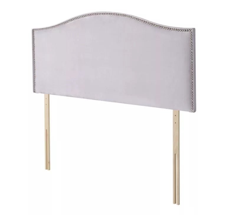 A light gray upholstered headboard with silver nailhead trim and wooden legs.