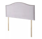A light gray upholstered headboard with silver nailhead trim and wooden legs.