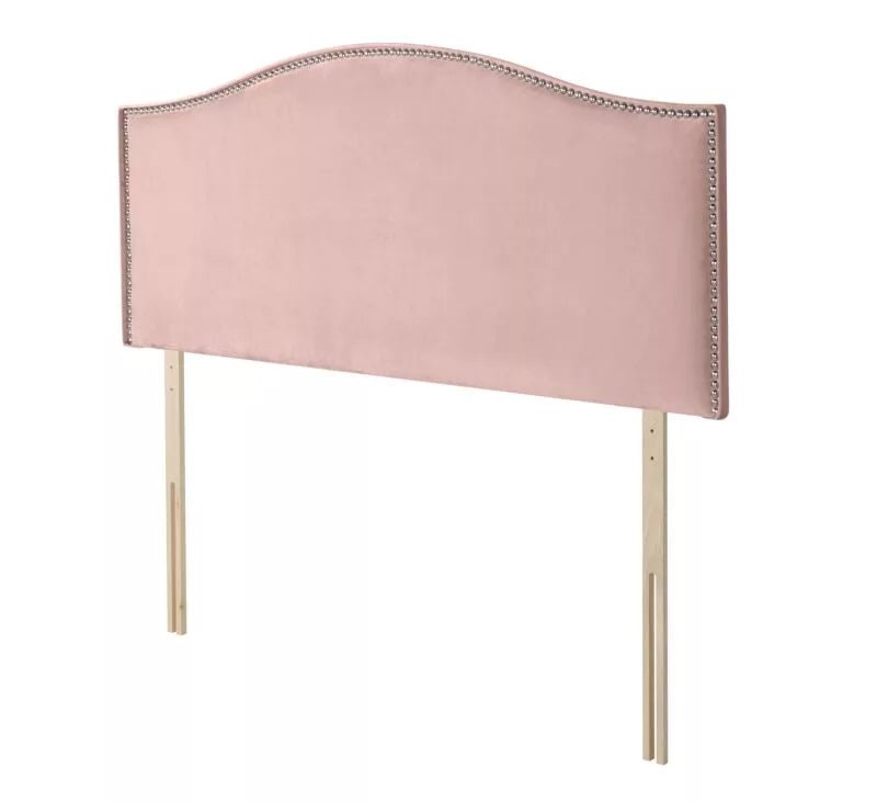 A pink velvet headboard with silver nailhead trim and wooden legs.