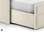 A stone white wooden underbed drawer pulled out from a bed frame.