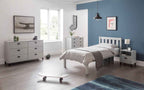 A white wooden bed frame with a grey blanket and pillows in a blue-walled bedroom.